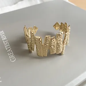 Close-up detail of a gold-colored textured open cuff bracelet with irregular jagged design