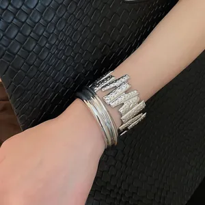 Close-up detail of a textured and smooth silver metal open cuff bracelet set on a wrist