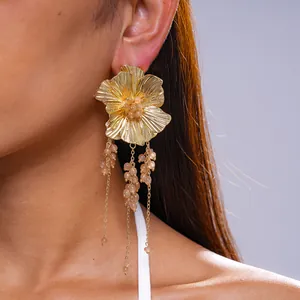 Detailweergave van gouden metalen bloemenoorknopjes met glazen kralenkwastjes op model.
