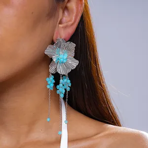 Detailweergave van grote zilveren bloemoorbellen met blauwe glazen kralenkwastjes bij model.
