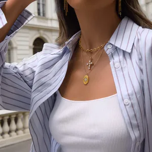 Detailed view of layered gold necklace with cross and starburst medallion pendants.