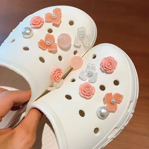 Primo piano di ciondoli per scarpe fai-da-te con rose e perle su sabot bianchi.