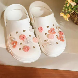 Dettaglio di ciondoli decorativi con rose rosa e perle su sabot bianchi classici