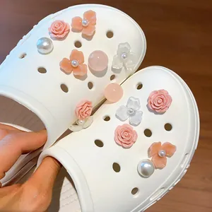Dettaglio di ciondoli rosa e perla attaccati a una scarpa clog bianca