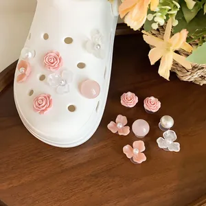Vista dettagliata di eleganti ciondoli a forma di rosa rosa e perla su uno zoccolo bianco.