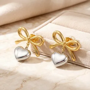 Detail view of two-tone stainless steel bow earrings with silver heart pendant charms