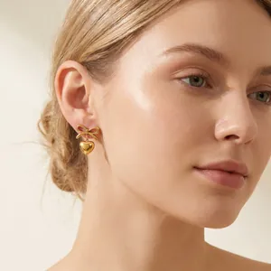 Close-up view of gold stainless steel bow and heart dangle earring worn by model