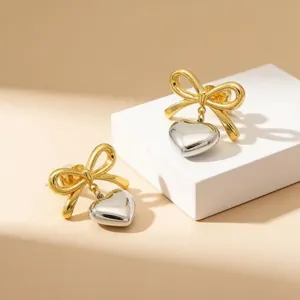 Close-up of two-tone stainless steel bow stud earrings with heart pendants on display
