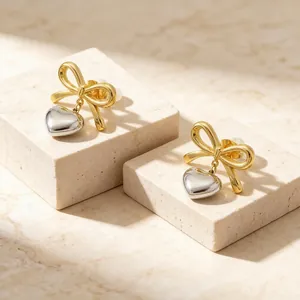Close-up detail of two-tone stainless steel bow earrings with hanging heart pendants