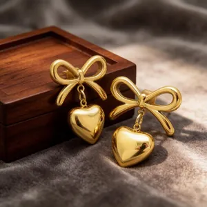 Macro view of golden stainless steel bow stud earrings with heart-shaped dangles on velvet
