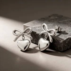 Close-up of elegant silver stainless steel bow earrings featuring a heart pendant charm