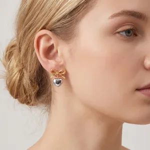 Close-up detail of a gold bow and silver heart pendant earring worn by a female model