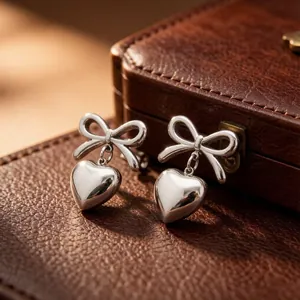 Close-up detail of stainless steel bow knot earrings with dangling heart pendant.