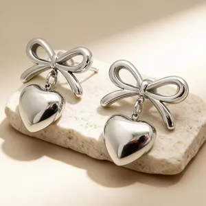 Detailed macro view of silver stainless steel bow earrings featuring heart-shaped pendants