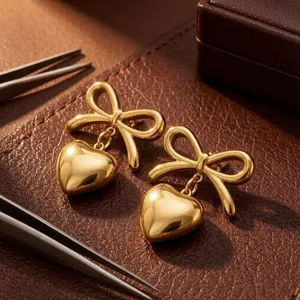 Detailed close-up of golden stainless steel bow heart earrings on a premium leather mat