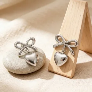 Close-up of silver stainless steel bow heart dangle earrings on a wooden display stand