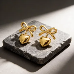 Detail of gold-colored stainless steel bow earrings with heart pendants on stone slab