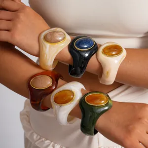 Bracciali grossi in acrilico marmorizzato con pietre ovali in resina sulle braccia moda.
