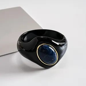 Primo piano di un bracciale rigido in acrilico nero con una pietra in resina marmorizzata blu