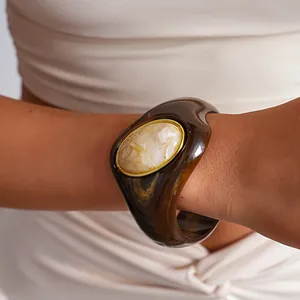 Primo piano di un bracciale rigido in acrilico marmorizzato con elemento ovale bianco.