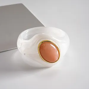 Dettaglio di un bracciale in acrilico bianco marmorizzato con pietra ovale pesca.
