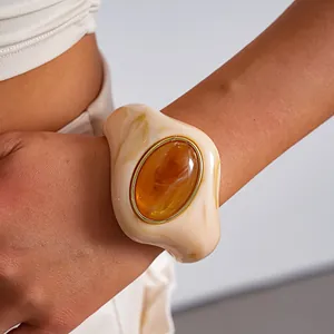 Dettaglio di un bracciale rigido in acrilico marmorizzato crema con pietra ambra.