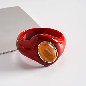 Dettaglio ravvicinato di un bracciale rigido rosso in acrilico con pietra ambra.