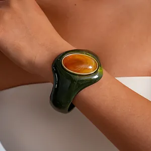 Dettaglio di un bracciale rigido in acrilico verde marmorizzato con intarsi in resina ambrata