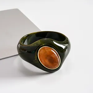 Dettaglio di bracciale rigido in acrilico verde scuro marmorizzato con pietra ambra.