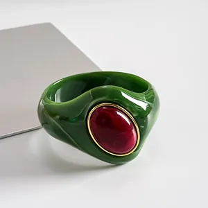 Vista dettagliata del bracciale rigido in acrilico verde marmorizzato con pietra rossa ovale.