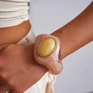 Dettaglio di un bracciale rigido in acrilico marmorizzato con elemento ovale dorato.