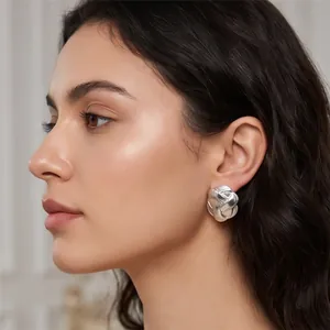 Close-up detail of silver stainless steel button earring with braided texture on model ear