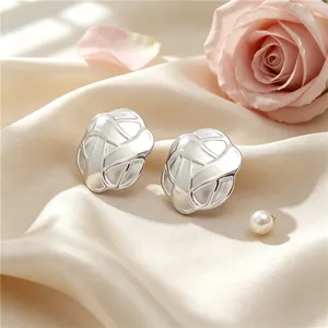 Close-up of silver-toned stainless steel button earrings with intricate lattice texture
