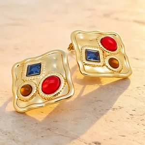 Gros plan de boucles d'oreilles dorées avec pierres multicolores sur fond de pierre naturelle.