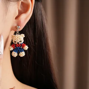 Close-up shot of a handmade beaded teddy bear drop earring worn by a model in a warm setting