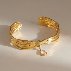 Detailed view of gold-plated wavy cuff bracelet with pear-cut zircon charm