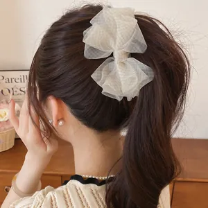 Dettaglio di un'elegante molletta per capelli con fiocco in organza in una coda di cavallo mossa.