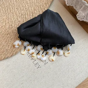 Dettaglio di una molletta per capelli in tessuto nero con nappe a conchiglia tonde.