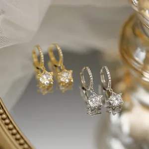 Detailansicht von Sternanhänger-Ohrringen in Gold und Silber mit funkelnden Steinen.