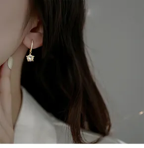 Nahaufnahme eines goldenen Creolen-Ohrrings mit Sternanhänger an einem Model-Ohr