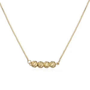 Close-up of minimalist gold-plated box chain necklace with four textured bead pendants