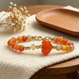 Bracciale minimalista in pietra naturale arancione con cuore e ciondolo a croce dorato.