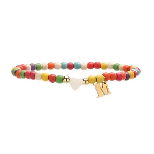 Détail d'une cheville en perles colorées avec un cœur blanc et une breloque en M