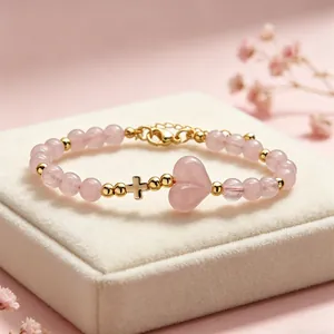 Dettaglio di bracciale con perle di quarzo rosa e ciondoli cuore e croce in oro su scatola.