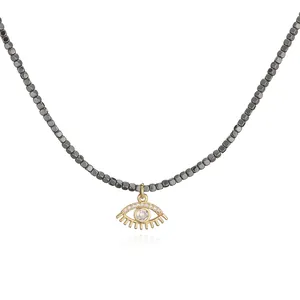 Macro view of a gold-plated evil eye pendant necklace with dark grey beaded chain