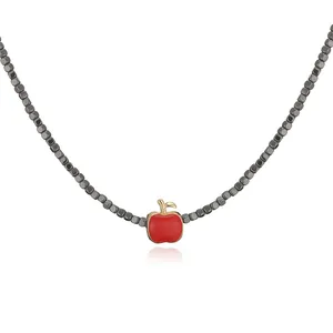 Detail view of a gold-plated necklace with a red apple pendant and black cube beads.