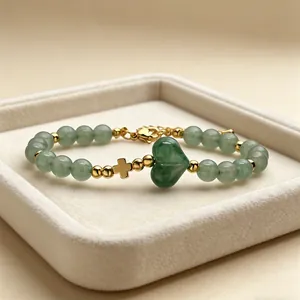 Primo piano di bracciale con perle di avventurina verde e ciondoli a cuore e croce d'oro.