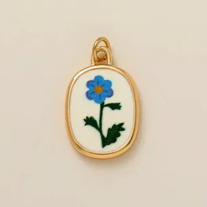 Close-up view of gold oval pendant featuring a blue flower pattern on a white base