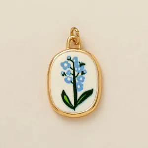 Close-up of an oval pendant featuring a delicate blue flower design in a gold-tone frame.