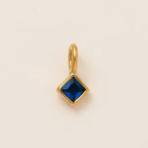 Detailed macro view of a square blue zircon birthstone charm in an 18K gold-plated setting